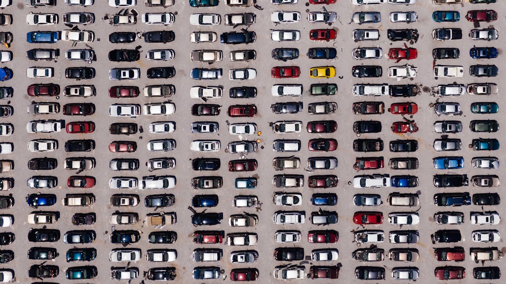 Top-down aerial shot of a large parking lot filled with rows of cars, showcasing organized symmetry.