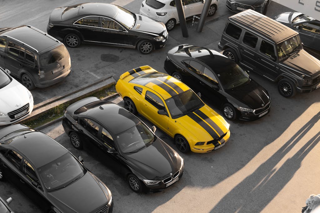 Top view of various cars parked in a parking lot, featuring a yellow sports car.