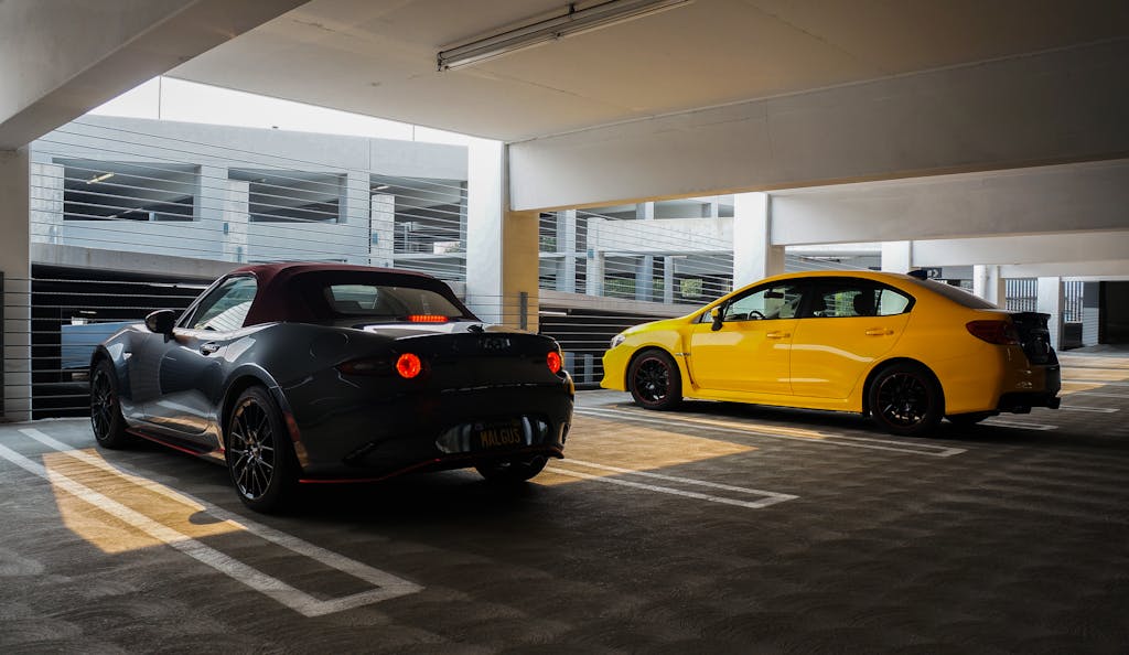 Two sports cars, Mazda and Subaru, parked in a sunlit indoor garage.